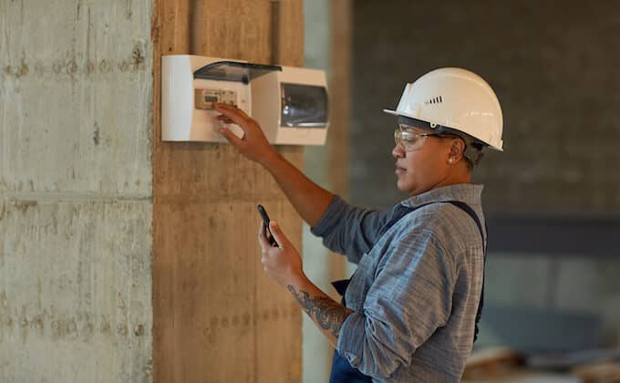 Side view portrait of female worker setting up electricity and using smartphone while working on construction site