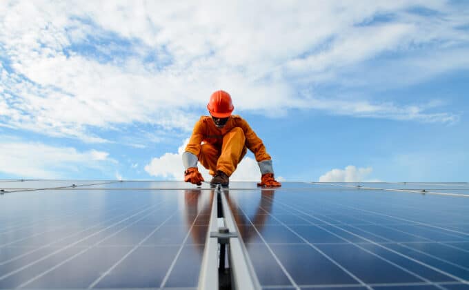 An installer, wearing an orange jumpsuit, finishes placing solar panels.