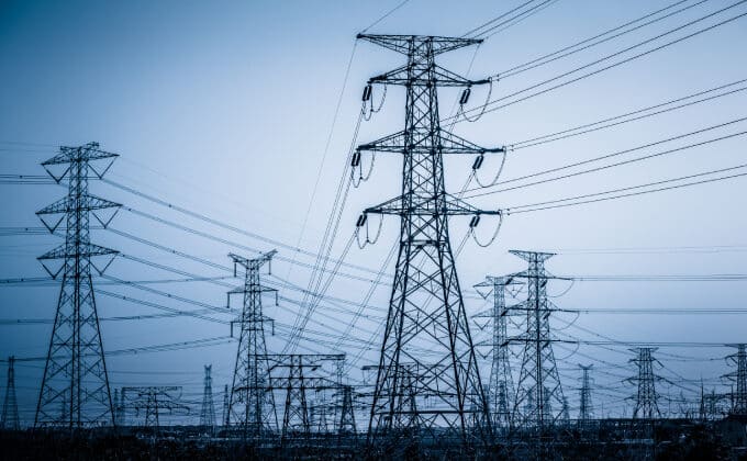 A grouping of electric transmission towers stand silhouetted against a grey-blue sky.