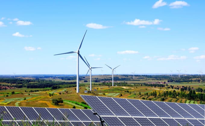 Solar panels and wind turbines in a rural field with a blue sky in the background.