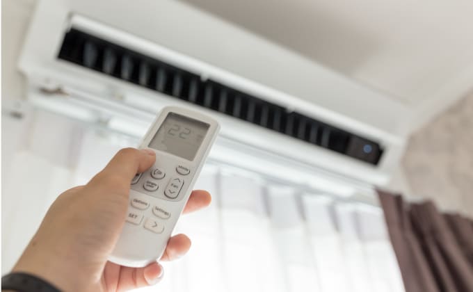 A hand holding a remote, adjusts an air conditioner.