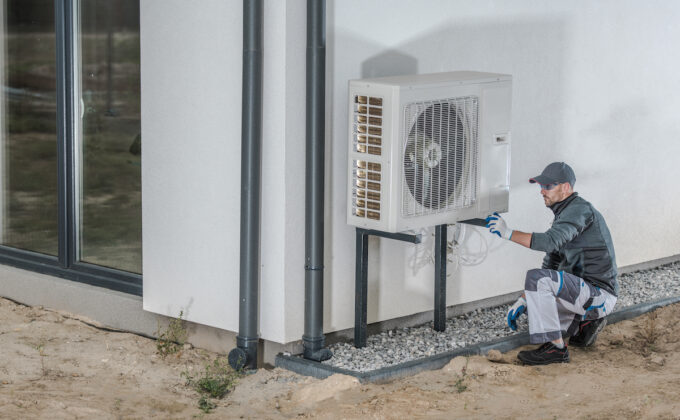 Worker kneeling next to heat pump when installing outside home