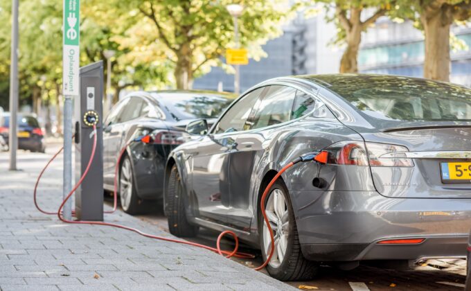 Two dark gray electric vehicles parked and charging at the side of a street