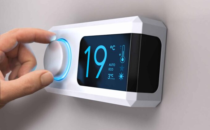 A white thermostat is installed on a beige wall. Its digital display indicates "19°C" in teal.