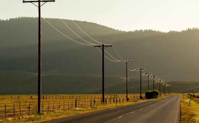 A row of power lines along a rural road with mountains in the background||Map of United States showing service areas of rural electric cooperatives