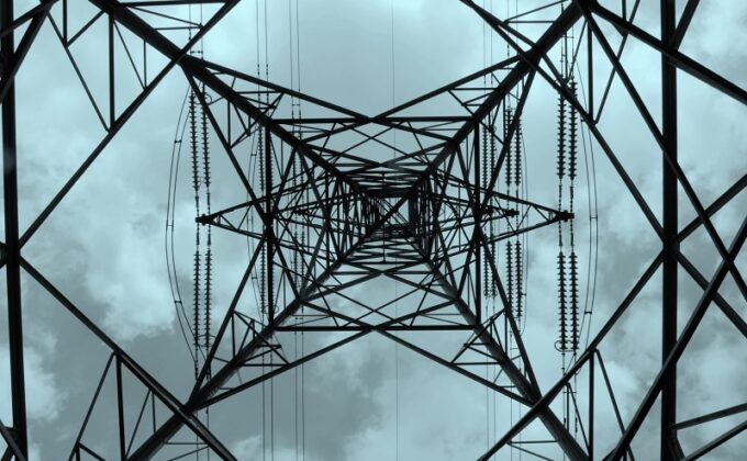 looking up a high-voltage power tower against cloudy sky