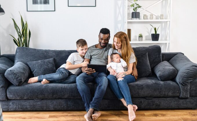 two adults and two children sitting on couch looking at tablet family