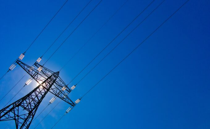 transmission tower against blue sky with sunlight beaming through