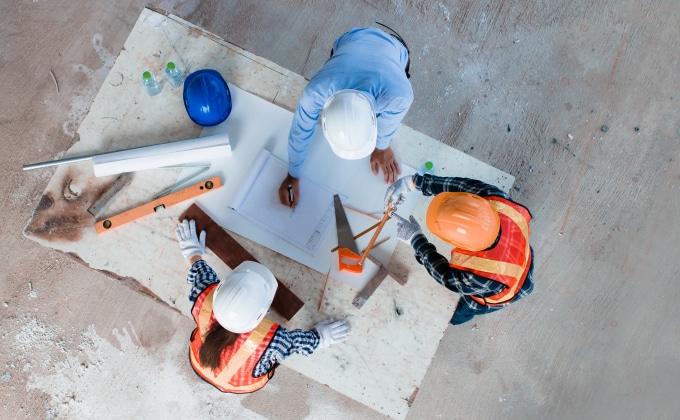 A group of engineers in hardhats stand over a table of blueprints.