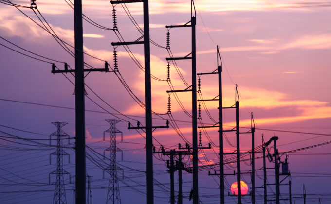 Silhouette of power distribution lines and towers against sunset