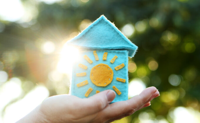 woman's hand holding up a small felt house with a sun on the front
