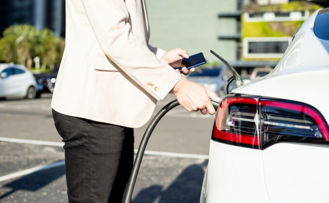 Mann schaut auf Handy bei einer Ladestation für Elektroauto Man looks at cell phone while charging electric vehicle|Mann schaut auf Handy bei einer Ladestation für Elektroauto Man looks at cell phone while charging electric vehicle