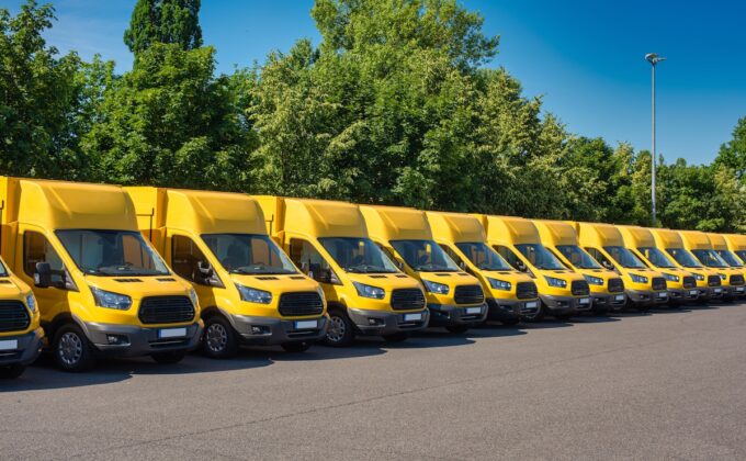 Row of yellow electric delivery vans parked in front of trees