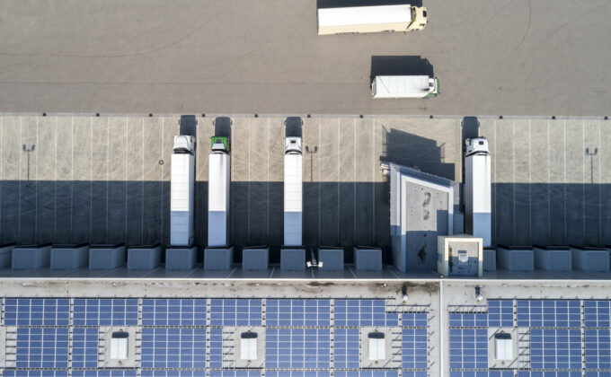 Aerial view of semi trucks during unloading and a large storehouse with solar panels on the rooftop.