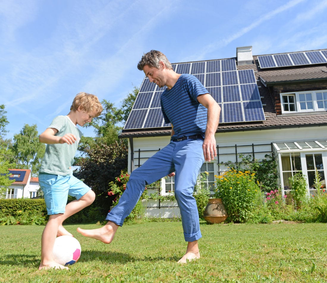 man and boy playing with a ball outside of a house with solar panels on its roof