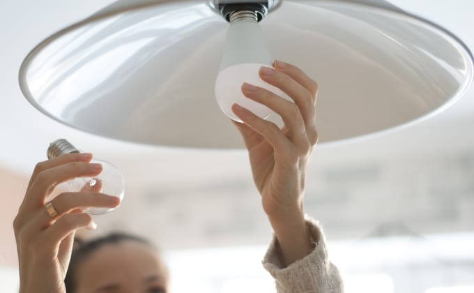 Hands reach up to replace a light bulb with an LED bulb.