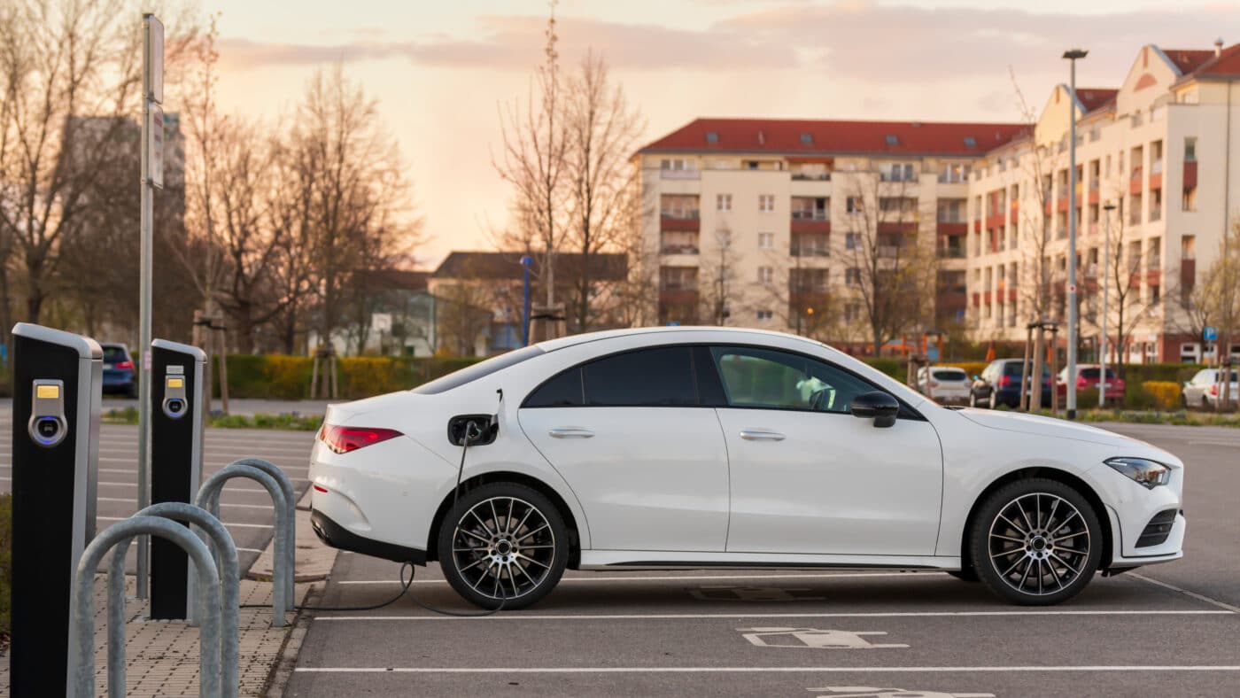 A white electric sedan charges in an apartment parking lot.