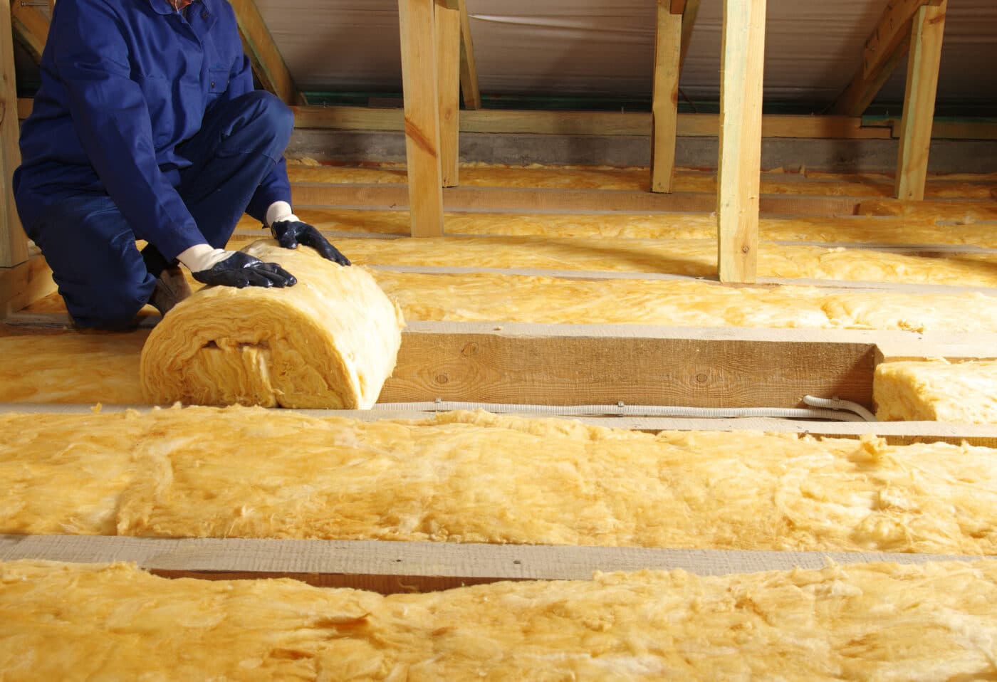 An installer completes unrolling a layer of insulation between wooden joists.