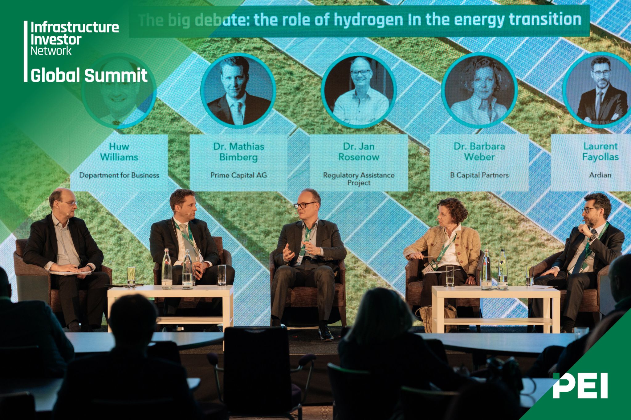 A group of five people sit on a stage in front of a screen projected backdrop. They are speakers on a panel for the Infrastructure Investor Network Global Summit. 