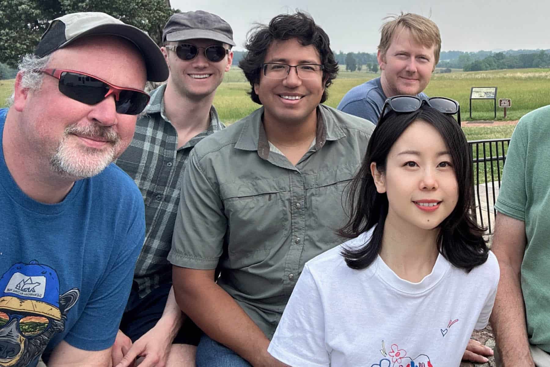 A group of six RAP colleagues visit Manassas National Battlefield Park in Virginia. They are smiling at the camera and wearing casual clothes. The park is behind them.