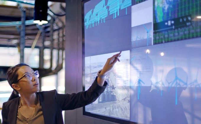 Young woman gesturing to large computer screen showing wind and solar energy