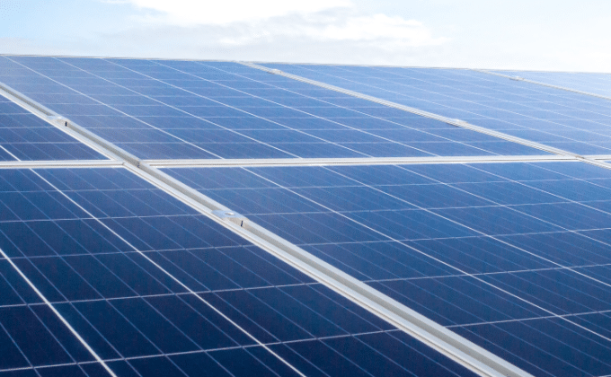 A close-up of solar panels filled the lower half of the image with a blue sky and clouds in the backgorund.