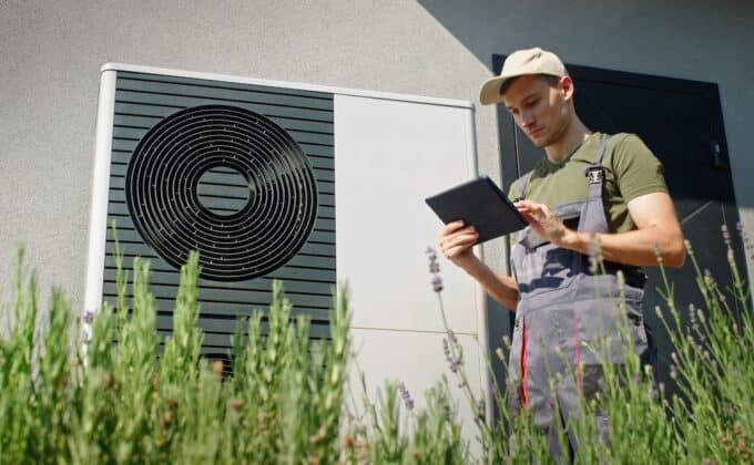 Technician using a tablet to inspect an outdoor heat pump unit on a sunny day.