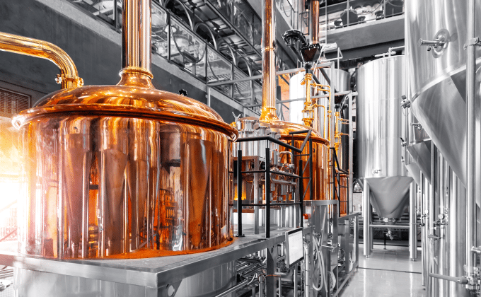 Copper vats in an industrial brewery shine in a ray of sunlight.
