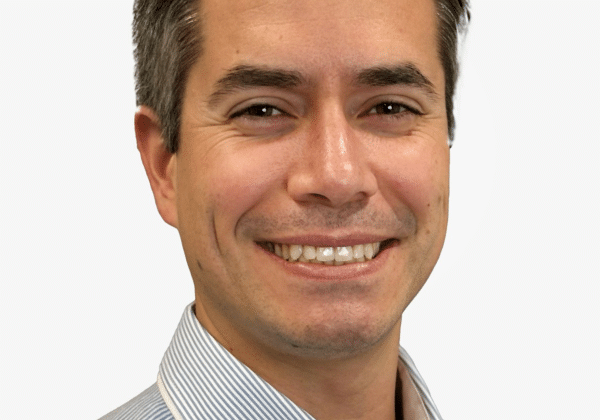 A man with short dark hair and medium-toned skin smiles at the camera. He is wearing a blue collared shirt.