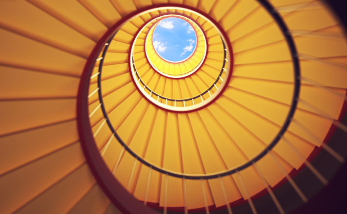An upward view of a spiral staircase mounting to a blue sky. Representing the looped approach of reducing grid costs.
